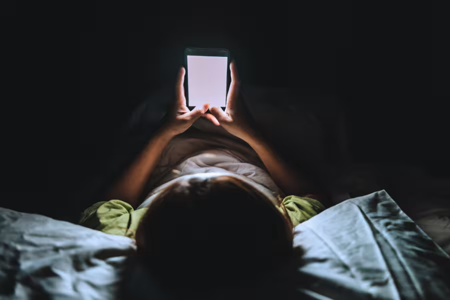 Zdjęcie dziecka leżącego na łóżku w ciemności przeglądającego telefon
