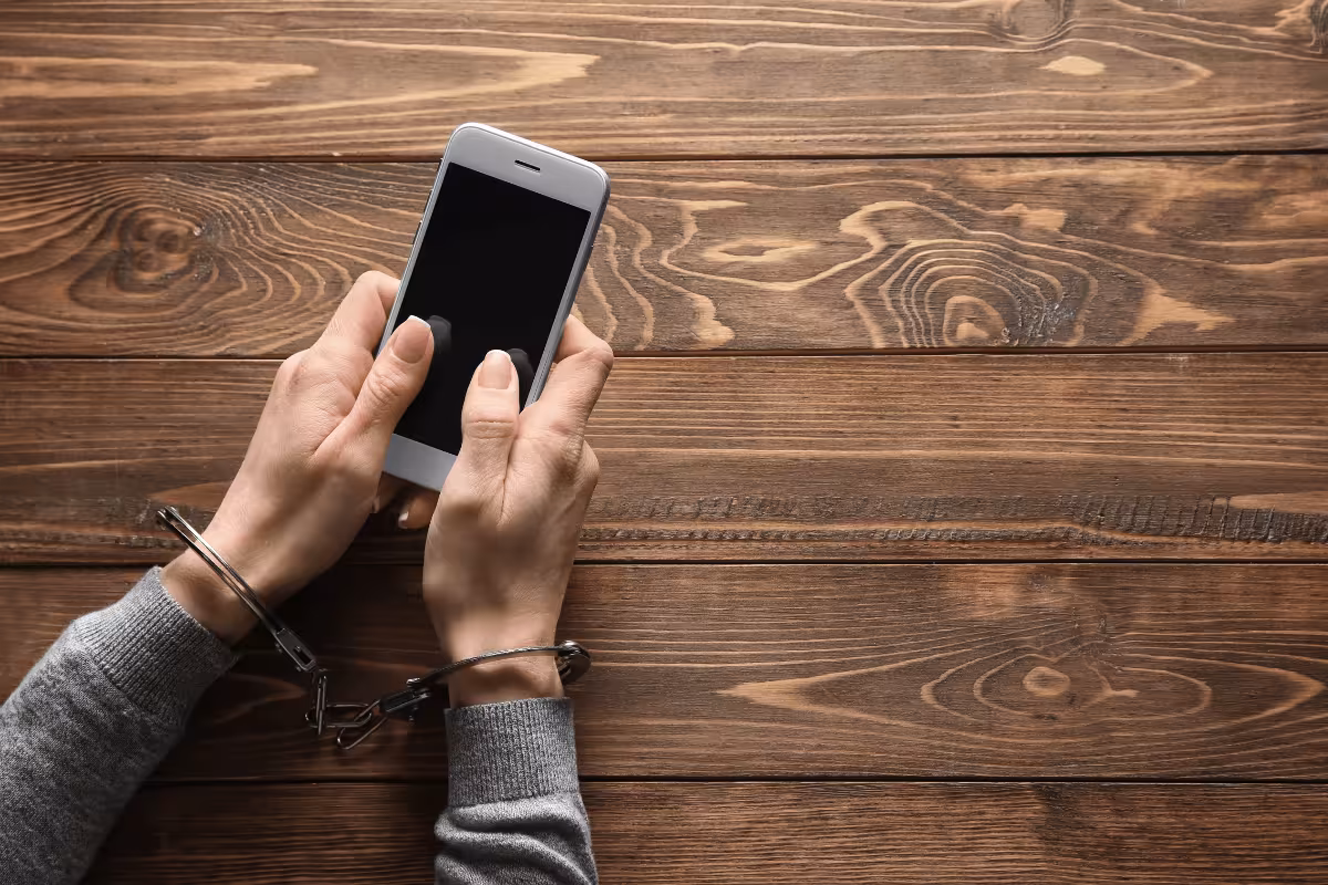 Zdjęcie przedstawiające ręce w kajdankach używające smartfon