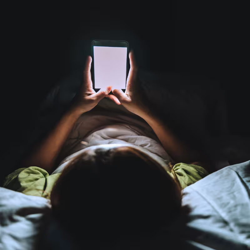 Zdjęcie dziecka leżącego na łóżku w ciemności przeglądającego telefon